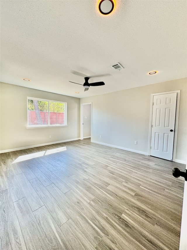 unfurnished room with a textured ceiling, light wood-type flooring, and ceiling fan