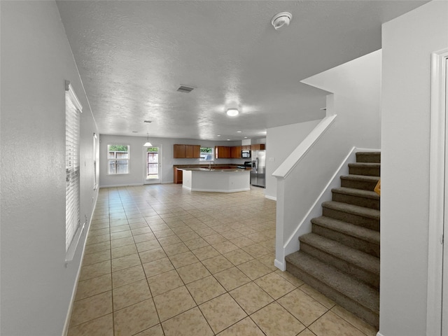 interior space featuring kitchen peninsula, stainless steel fridge, light tile patterned floors, a textured ceiling, and pendant lighting