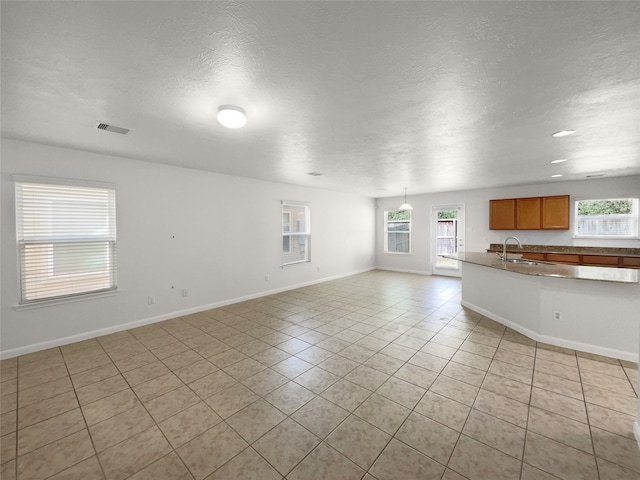 unfurnished living room with sink, a textured ceiling, and light tile patterned flooring