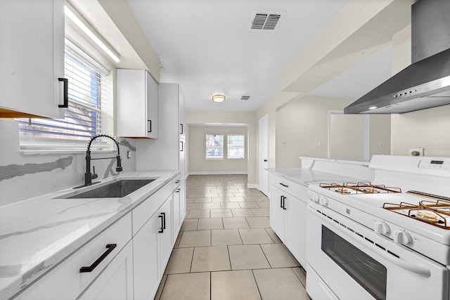 kitchen featuring white gas range, white cabinetry, light stone countertops, wall chimney exhaust hood, and sink