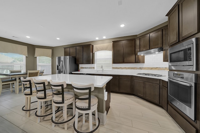 kitchen with decorative backsplash, a kitchen island, appliances with stainless steel finishes, dark brown cabinetry, and sink