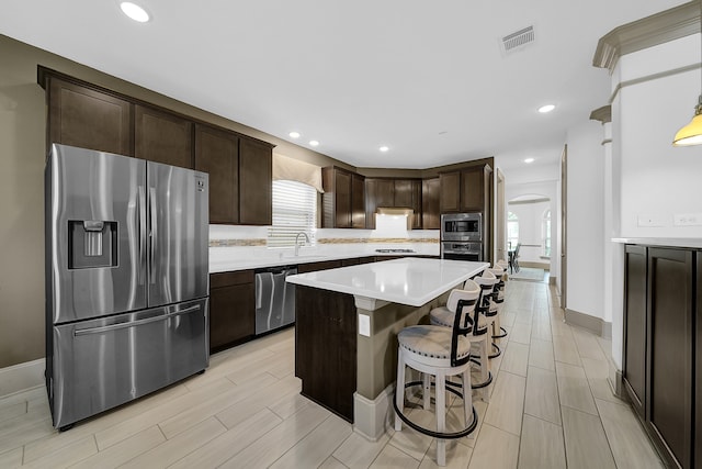 kitchen featuring appliances with stainless steel finishes, dark brown cabinetry, a center island, and a kitchen bar