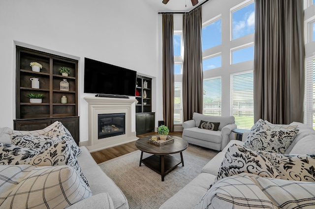 living room featuring a high ceiling, light hardwood / wood-style flooring, built in shelves, and ceiling fan