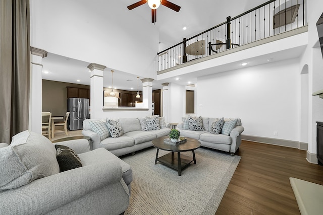 living room featuring ceiling fan, dark wood-type flooring, a high ceiling, and decorative columns