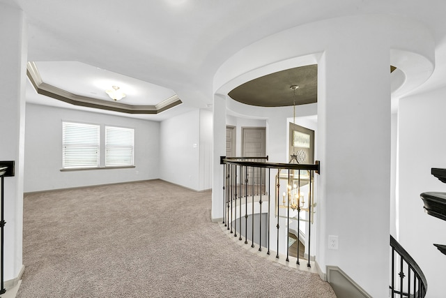 hallway featuring light carpet, ornamental molding, and a tray ceiling