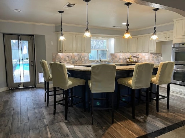 kitchen with light stone counters, stainless steel double oven, white cabinets, hanging light fixtures, and a breakfast bar area