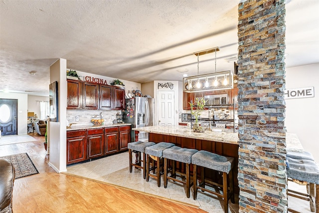 kitchen featuring a breakfast bar, light stone counters, hanging light fixtures, appliances with stainless steel finishes, and light hardwood / wood-style floors