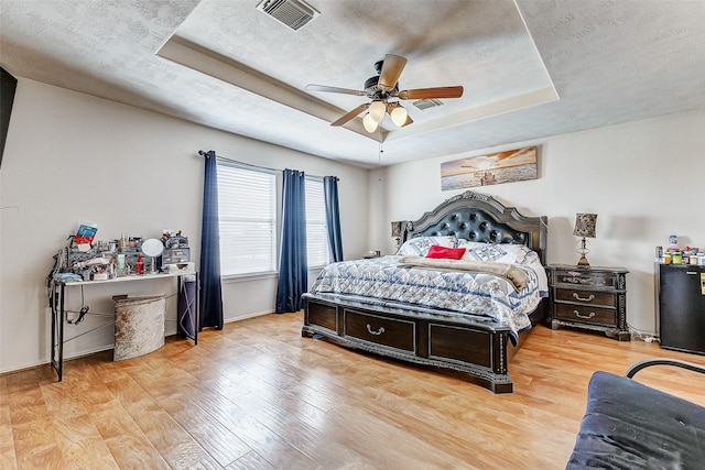 bedroom with a raised ceiling, ceiling fan, and light hardwood / wood-style floors