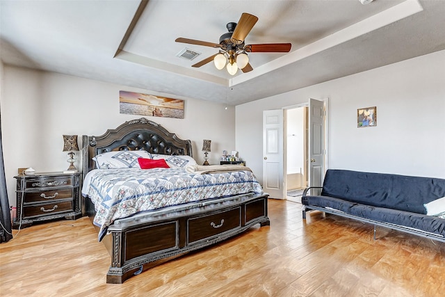 bedroom with ceiling fan, a tray ceiling, and light hardwood / wood-style flooring