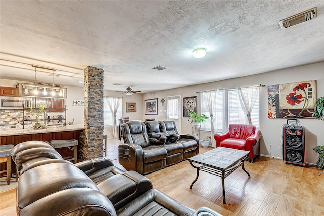 living room with ceiling fan, light hardwood / wood-style floors, a textured ceiling, and ornate columns