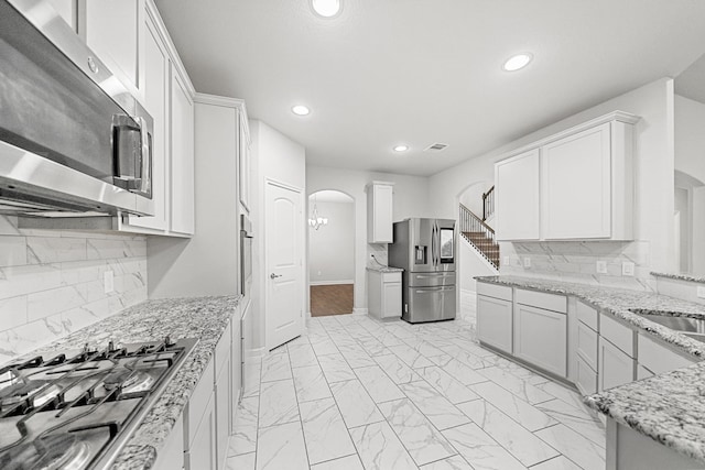 kitchen featuring white cabinetry, light stone counters, stainless steel appliances, and decorative backsplash