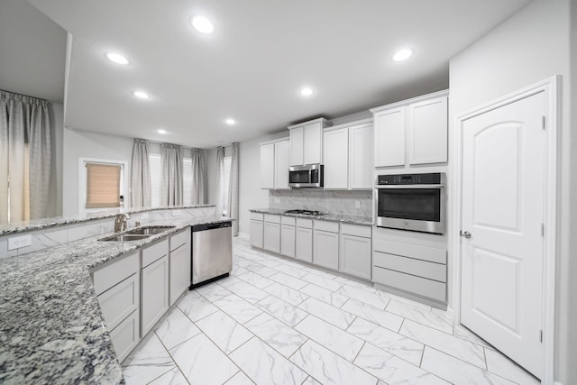 kitchen featuring tasteful backsplash, light stone counters, white cabinetry, sink, and stainless steel appliances