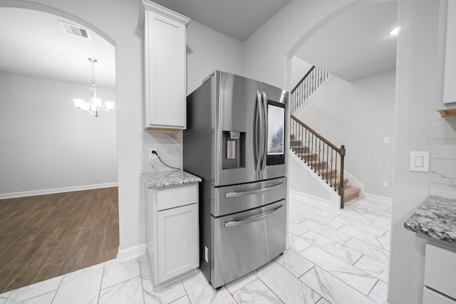 kitchen with hanging light fixtures, white cabinetry, light stone countertops, light hardwood / wood-style flooring, and stainless steel refrigerator with ice dispenser