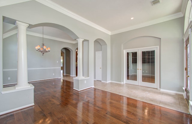 unfurnished living room with an inviting chandelier, hardwood / wood-style flooring, crown molding, ornate columns, and french doors