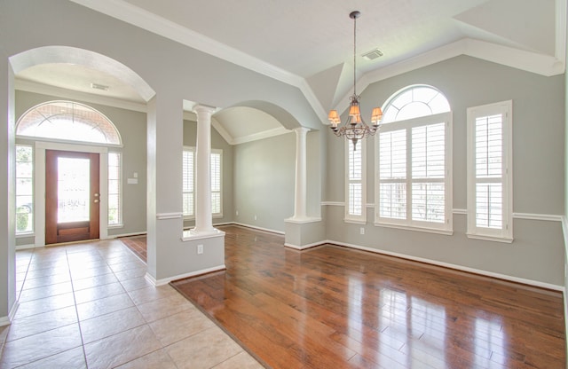 foyer featuring ornate columns, light hardwood / wood-style floors, lofted ceiling, crown molding, and an inviting chandelier