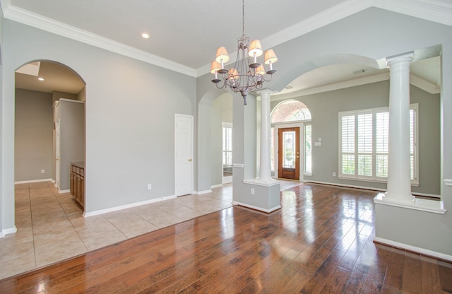 interior space featuring lofted ceiling, light hardwood / wood-style flooring, ornamental molding, decorative columns, and an inviting chandelier