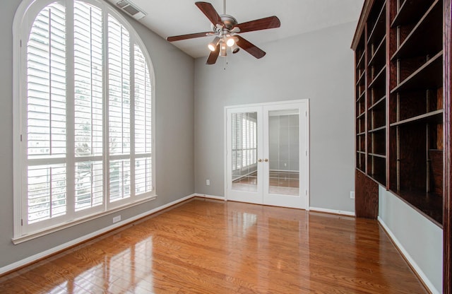 empty room with wood finished floors, visible vents, a ceiling fan, french doors, and baseboards