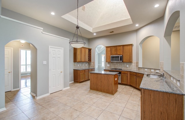 kitchen featuring decorative backsplash, kitchen peninsula, a tray ceiling, pendant lighting, and appliances with stainless steel finishes