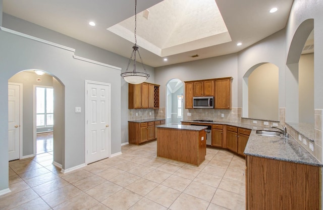 kitchen featuring tasteful backsplash, a center island, a sink, brown cabinetry, and stainless steel microwave