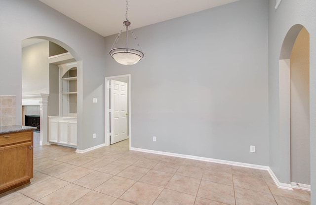 unfurnished dining area with a fireplace, high vaulted ceiling, baseboards, and light tile patterned floors