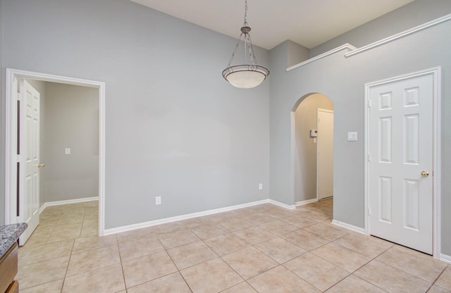 unfurnished room with arched walkways, a high ceiling, baseboards, and light tile patterned floors