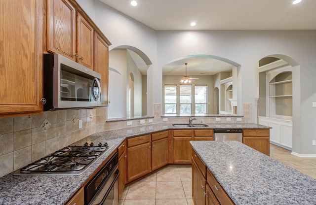 kitchen with stainless steel appliances, a ceiling fan, light tile patterned floors, light stone countertops, and brown cabinetry