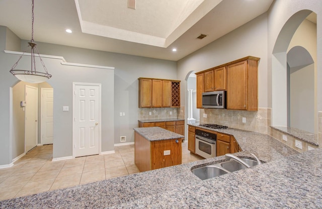 kitchen featuring brown cabinetry, arched walkways, appliances with stainless steel finishes, and a sink