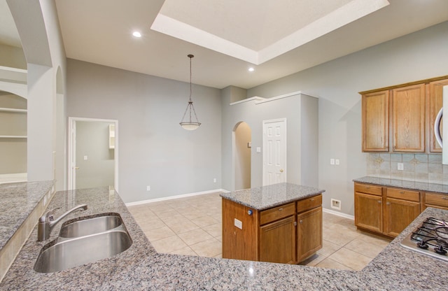 kitchen with tasteful backsplash, a kitchen island, stainless steel gas stovetop, pendant lighting, and sink