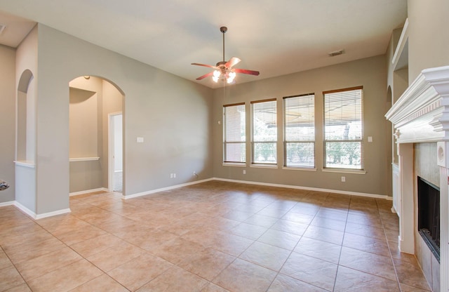 unfurnished living room featuring arched walkways, visible vents, ceiling fan, a fireplace, and light tile patterned floors
