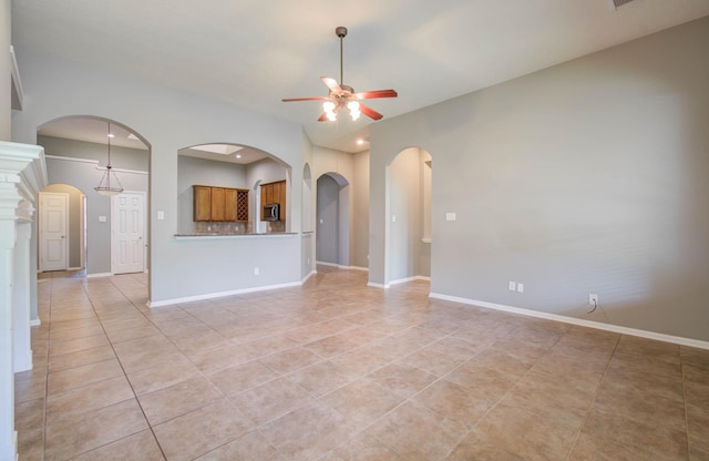 empty room featuring baseboards, arched walkways, ceiling fan, and light tile patterned flooring