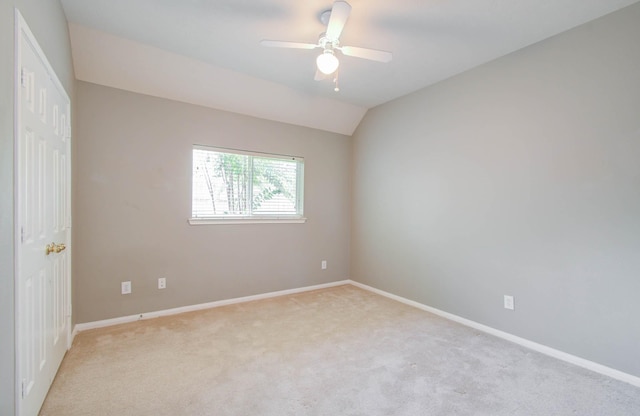 empty room featuring light carpet, a ceiling fan, vaulted ceiling, and baseboards