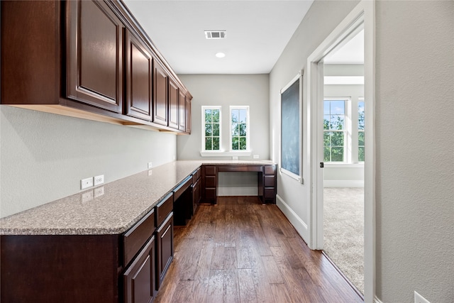 kitchen with built in desk, dark wood-type flooring, light stone countertops, and dark brown cabinetry