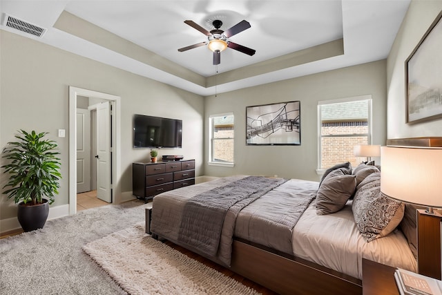 bedroom with a raised ceiling, multiple windows, and ceiling fan