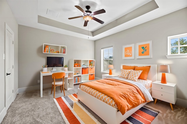 carpeted bedroom with ceiling fan and a raised ceiling