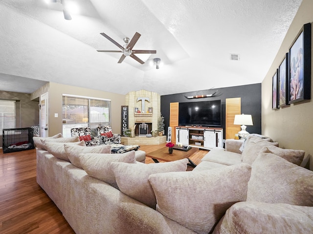 living room with a fireplace, a textured ceiling, ceiling fan, vaulted ceiling, and dark wood-type flooring