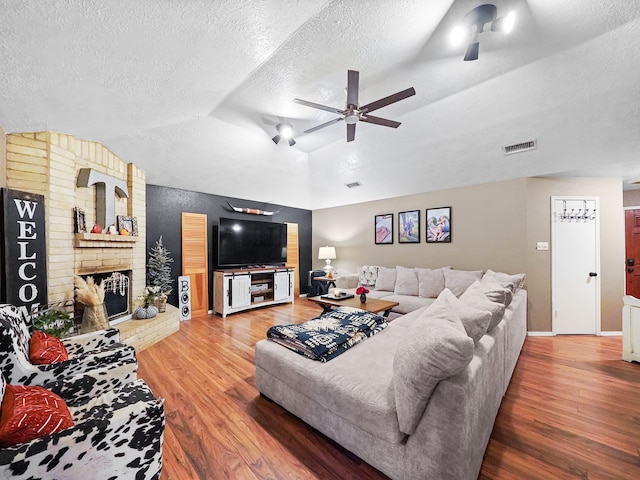 living room with a fireplace, a textured ceiling, hardwood / wood-style floors, ceiling fan, and lofted ceiling