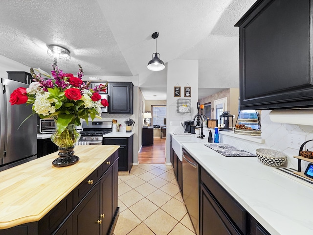 kitchen featuring a textured ceiling, stainless steel appliances, hanging light fixtures, and sink