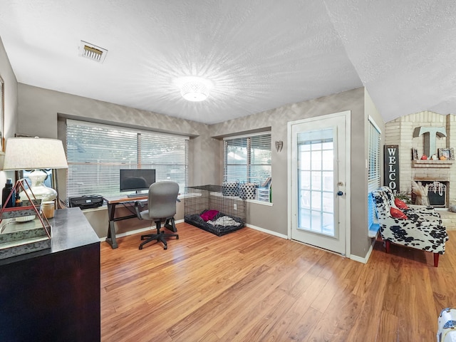 home office with lofted ceiling, a textured ceiling, wood-type flooring, and a fireplace