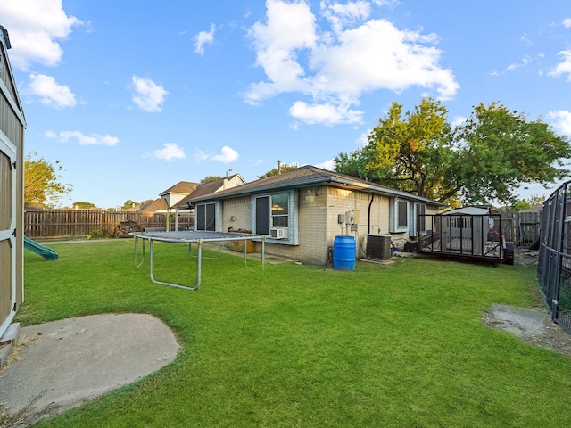 rear view of house with central air condition unit, a patio area, a yard, and a trampoline