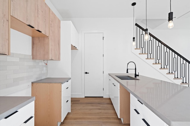 kitchen with white cabinetry, sink, hanging light fixtures, light hardwood / wood-style flooring, and decorative backsplash