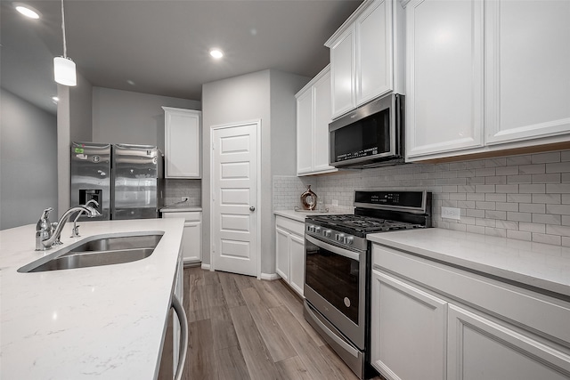 kitchen featuring sink, white cabinetry, stainless steel appliances, pendant lighting, and light hardwood / wood-style flooring