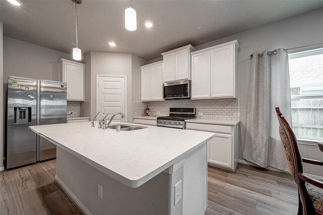 kitchen with appliances with stainless steel finishes, light hardwood / wood-style flooring, white cabinetry, and hanging light fixtures