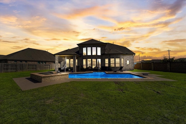 back house at dusk featuring a patio, a fenced in pool, and a lawn