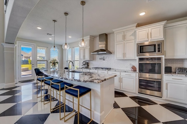 kitchen featuring sink, an island with sink, wall chimney range hood, and stainless steel appliances