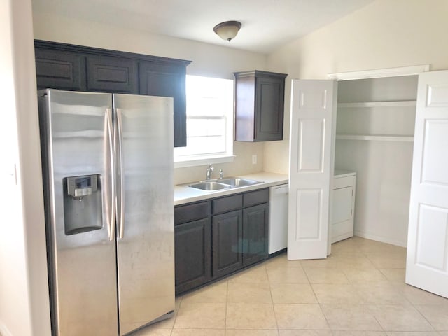 kitchen featuring washer / clothes dryer, sink, white dishwasher, light tile patterned floors, and stainless steel refrigerator with ice dispenser