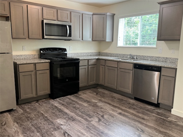 kitchen with stainless steel appliances, light stone counters, dark hardwood / wood-style floors, and sink