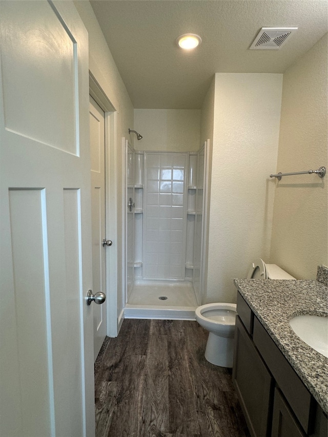 bathroom with walk in shower, vanity, a textured ceiling, hardwood / wood-style floors, and toilet