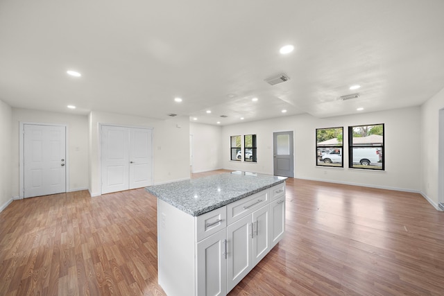 kitchen with light hardwood / wood-style floors, a center island, white cabinetry, and light stone counters