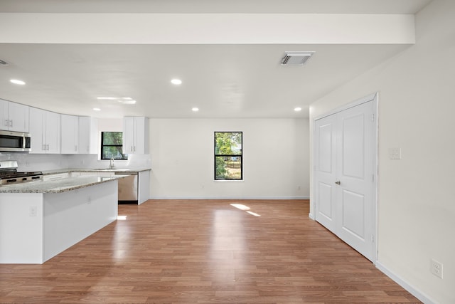 kitchen featuring appliances with stainless steel finishes, white cabinetry, light hardwood / wood-style flooring, sink, and light stone counters