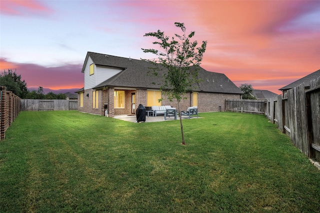 back house at dusk with a patio, an outdoor living space, and a lawn